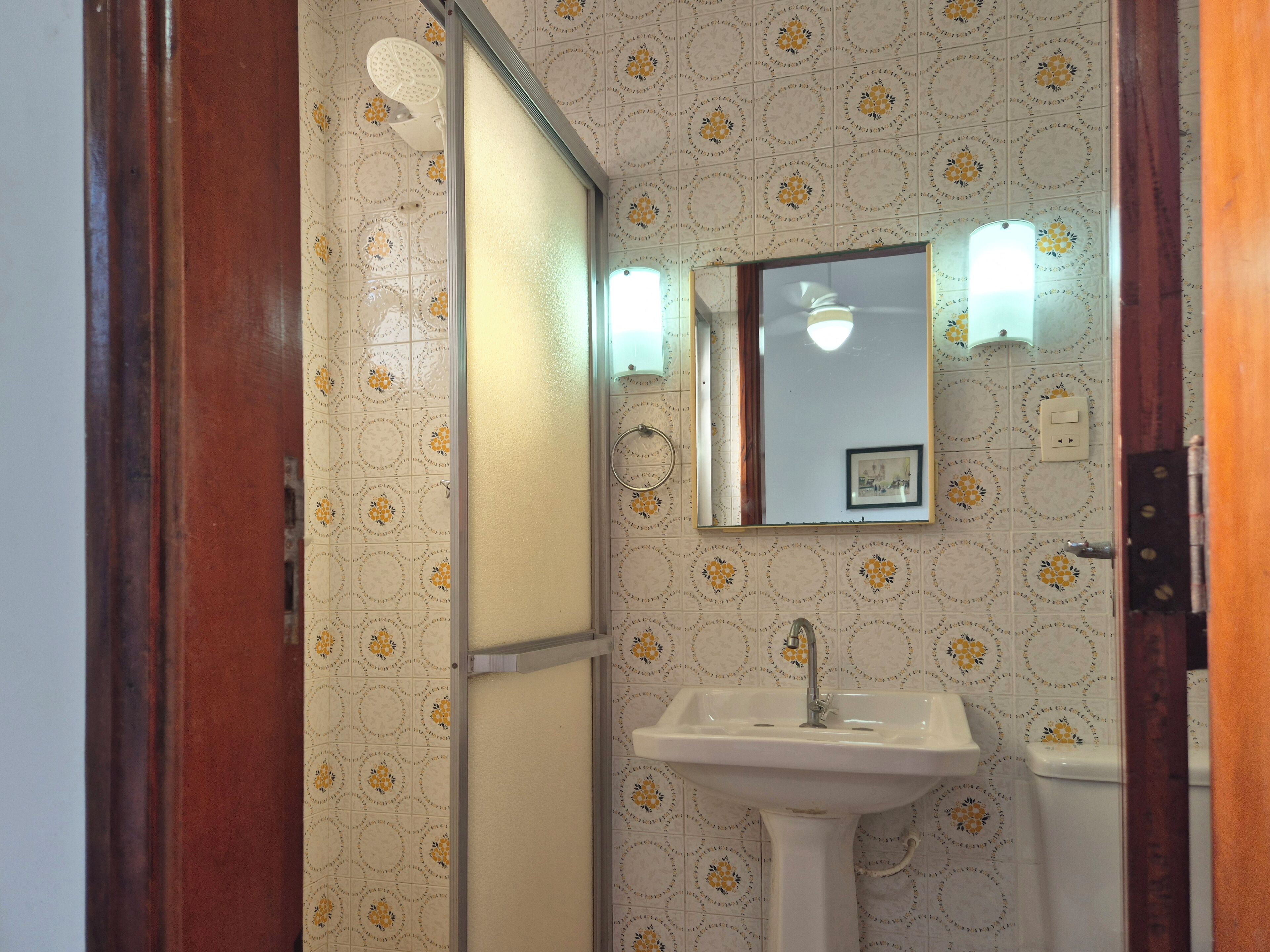 Casa de banho com lavatório branco, espelho e cabine de duche.