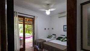 A room with two beds, a ceiling fan, an air conditioning unit, and a view of a garden through a glass door. - HOSTEL QUINTAL GUEST - Guarujá (Guarujá)