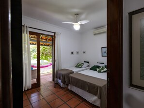 A room with two beds, a ceiling fan, an air conditioning unit, and a view of a garden through a glass door. - HOSTEL QUINTAL GUEST - Guarujá (Guarujá)
