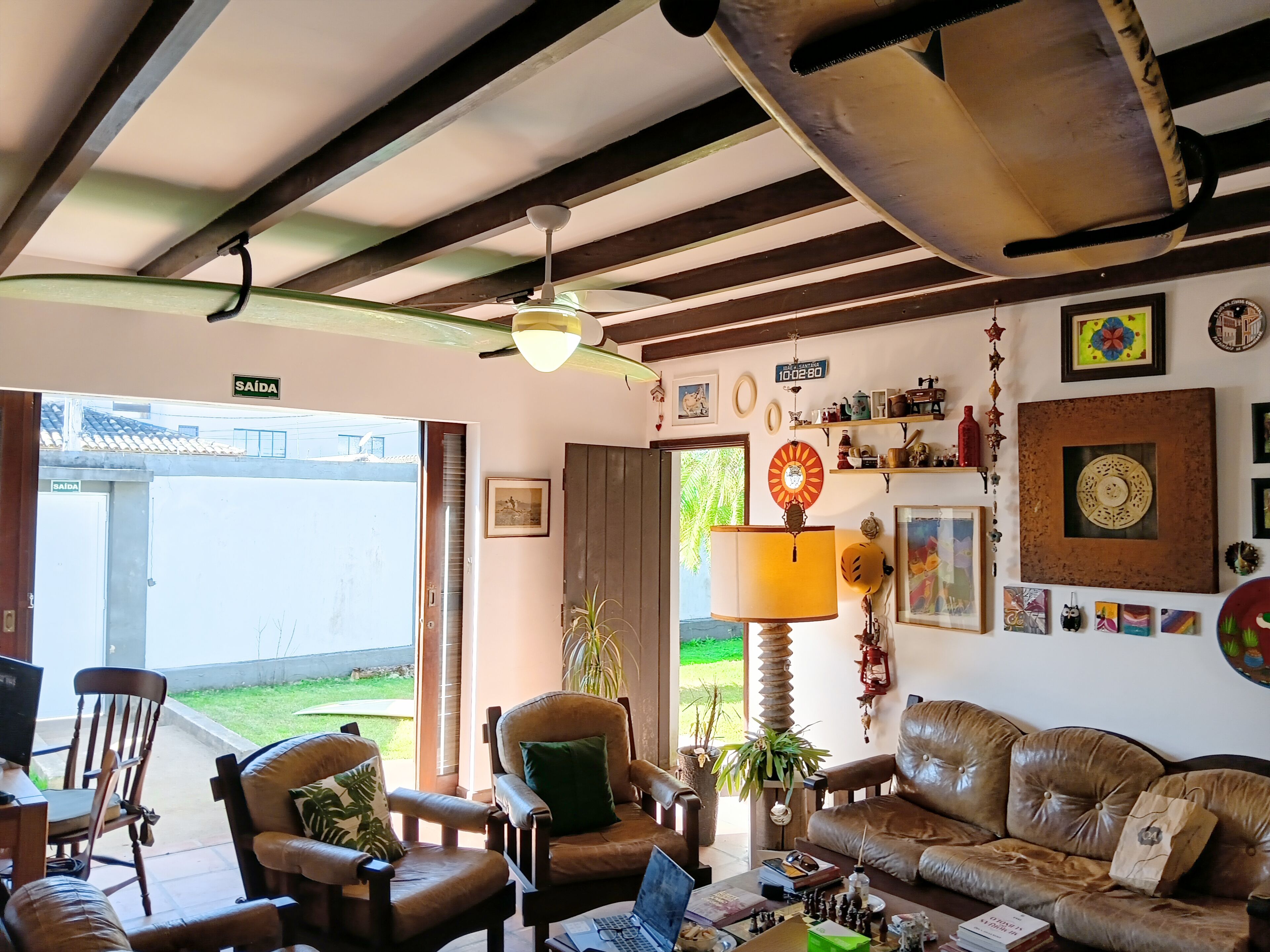 A cozy living room with a sofa, chairs, a table with books and a chess set, a lamp, and a ceiling fan.