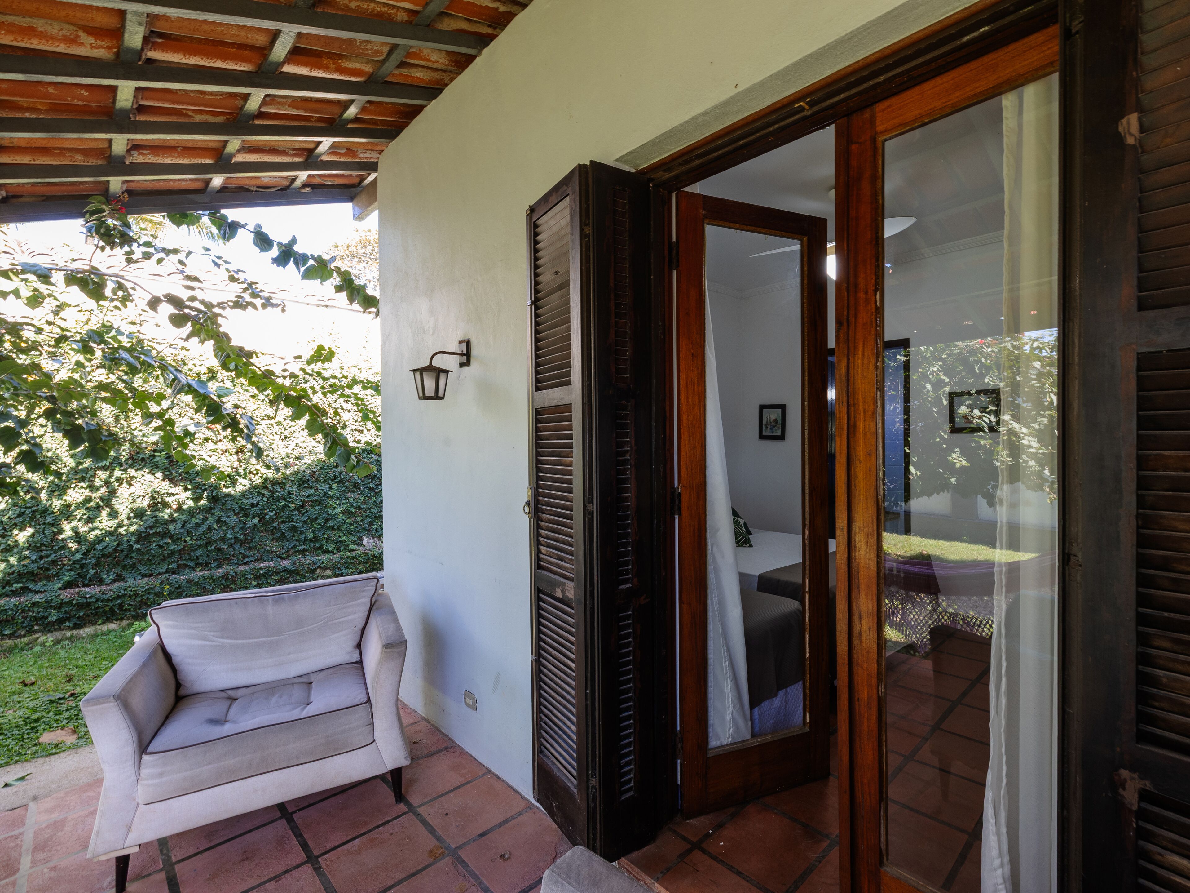 A covered patio area with a sofa, a sliding glass door leading to a bedroom, and a wall-mounted light fixture.