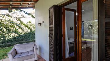 Ein überdachter Patio-Bereich mit einer Couch, einer Glasschiebetür, die zu einem Schlafzimmer führt, und einer Wandleuchte.