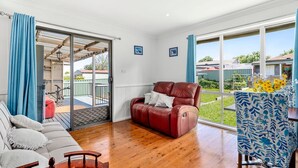 Un salon spacieux avec un canapé en cuir, une table basse en bois et une vue sur le jardin à travers de grandes fenêtres.