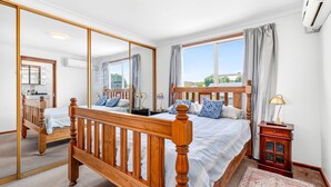 Une chambre avec un grand miroir, un lit en bois, des lampes de chevet et une vue sur l’extérieur.