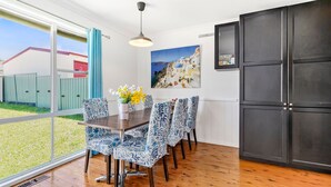 Un coin repas avec une table et des chaises, un meuble noir et un tableau représentant un paysage côtier.