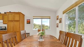 A dining area with a wooden table, chairs, a vase with flowers, and a window with a view of trees. - Yosemite Terrace View Retreat (Mariposa)