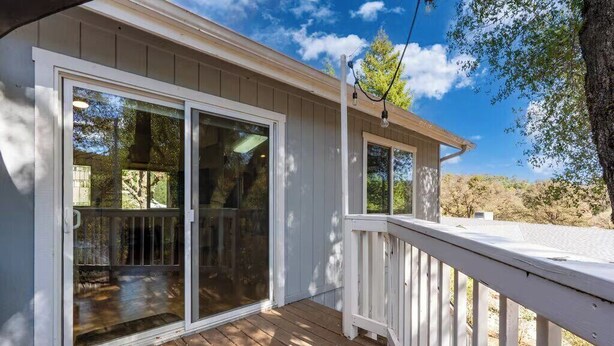 A wooden deck with a white railing, a sliding glass door, and a clear view of the surrounding trees and sky. - Yosemite Terrace View Retreat (Mariposa)