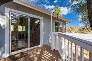 A wooden deck with a white railing, a sliding glass door, and a clear view of the surrounding trees and sky. - Yosemite Terrace View Retreat (Mariposa)