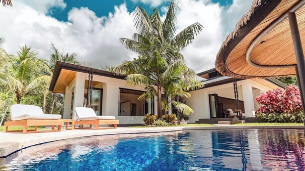 Un complexe hôtelier moderne doté d’une piscine, de chaises longues et d’un aménagement paysager de style tropical.