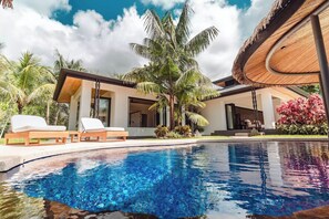 Una moderna località turistica con piscina, lettini e vegetazione tropicale.