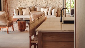 Un intérieur moderne avec un mur en pierre, un plafond en bois, un canapé, des fauteuils en osier et un coin repas.