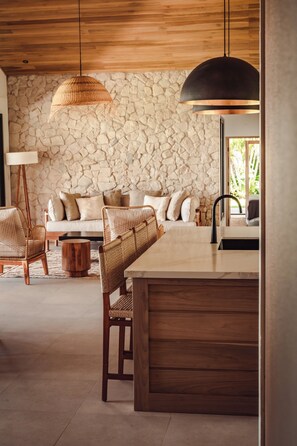 A modern interior with a stone wall, wooden ceiling, a sofa, wicker chairs, and a dining area. - Casa Palmera Azul (Osa)