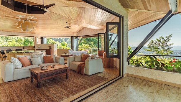 Amplia sala de estar con techo de madera, ventanas grandes y vista a zonas verdes.