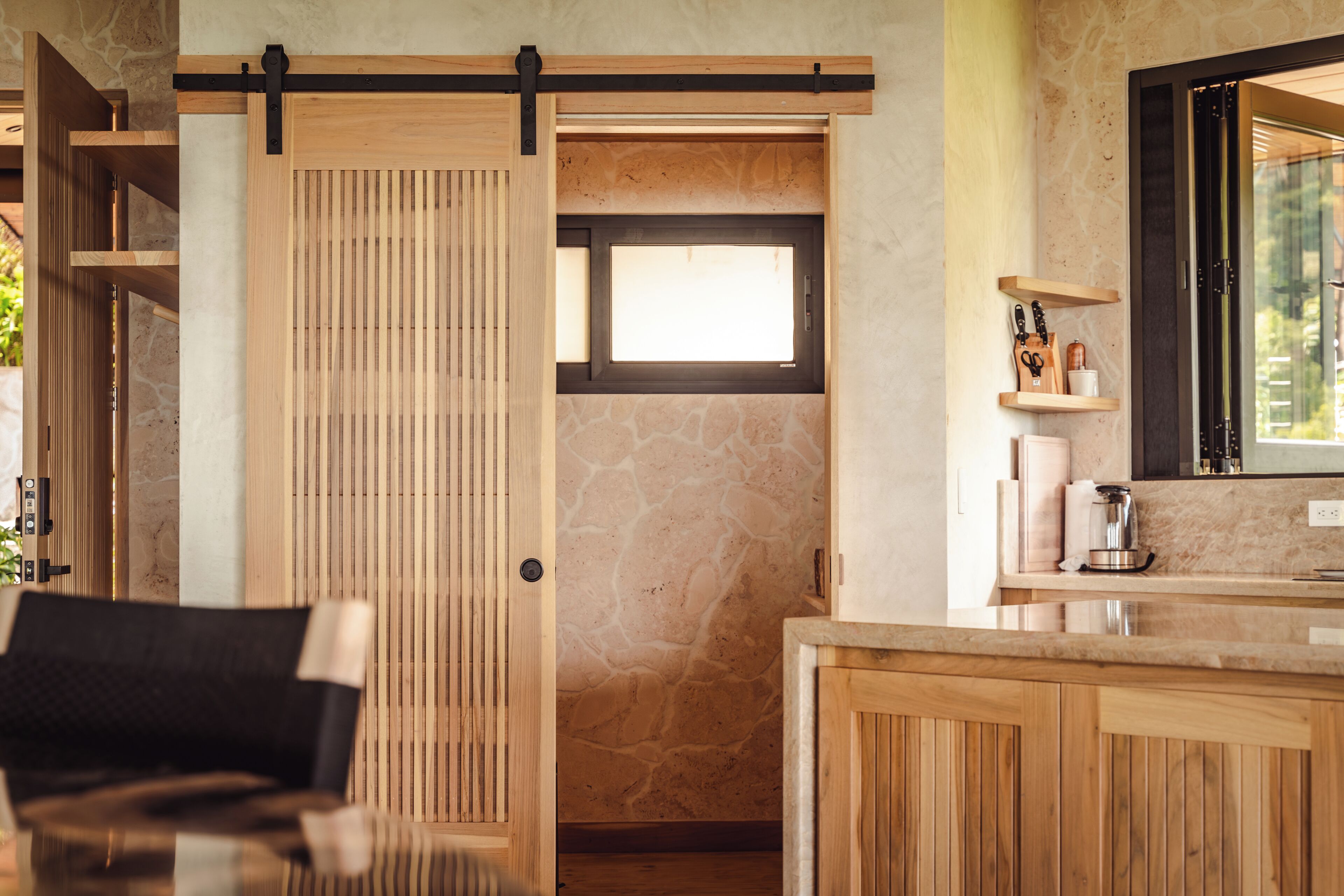 A room with a sliding wooden door, a stone wall, a wooden counter, and a window.