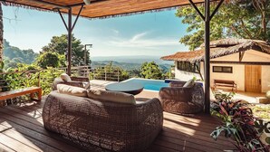 Una terraza de madera con mobiliario de mimbre, una piscina y vistas al paisaje.