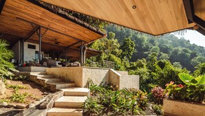 Una estructura de madera con techo de paja, escalones de piedra y abundante vegetación al fondo.