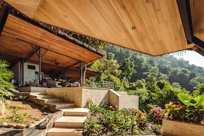 A wooden structure with a thatched roof, stone steps, and lush greenery in the background.