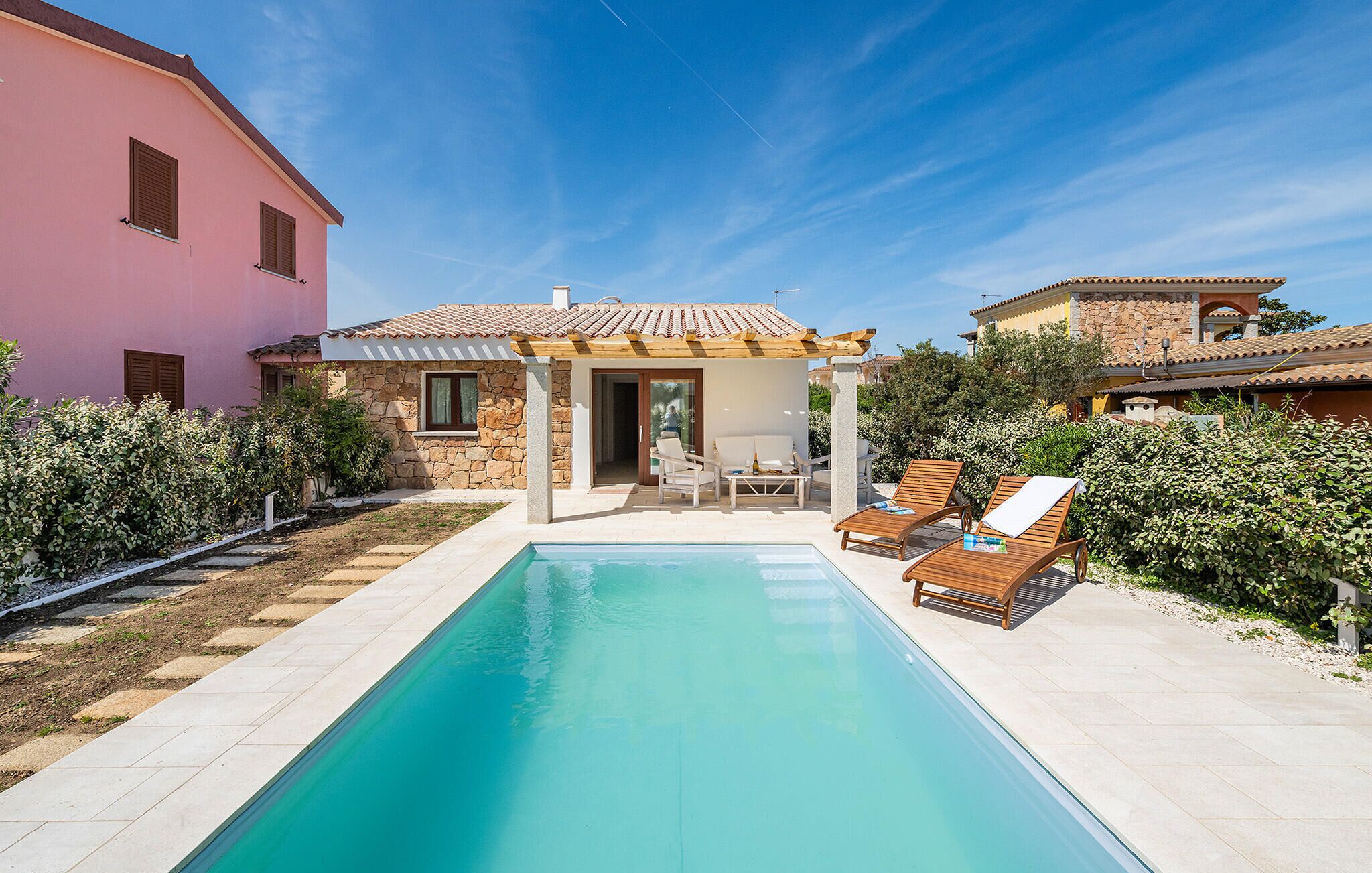 A poolside area with a stone building, a pergola, and lounge chairs.