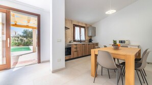 A modern kitchen with wooden cabinets, a dining table with chairs, and a view of a pool outside. - Nice home in San Teodoro (San Teodoro)