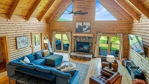 A log cabin interior with a sofa, coffee table, fireplace, and large windows. - Grand Mountain Lodge, Pickleball, Barrel Sauna, Hot Tub, Game Room, Arcade (Luray)