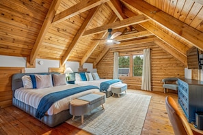 A wooden cabin bedroom with a large bed, two bedside tables, a desk, and a window.