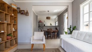 A spacious living room with a white sofa, a wooden bookshelf, and a dining area with a table and chairs. - Casa em Buzios com Piscina perto da Praia (Armação dos Búzios)