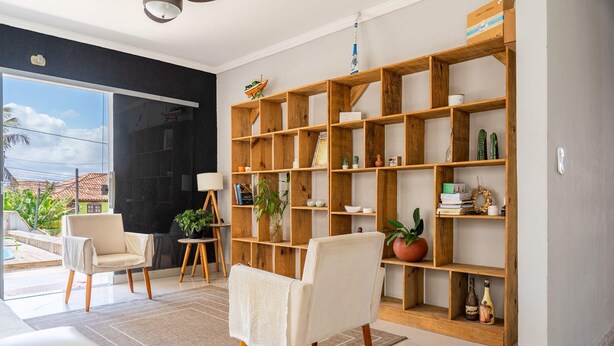 A modern living room with a large bookshelf, two armchairs, a coffee table, and a view of the outside. - Casa em Buzios com Piscina perto da Praia (Armação dos Búzios)