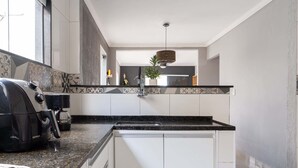 A modern kitchen with a built-in espresso machine, a sink, and a decorative hanging light fixture. - Casa em Buzios com Piscina perto da Praia (Armação dos Búzios)