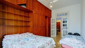 A bedroom with two beds, wooden wardrobes, and a white door leading to a dining area. - Apto no Rio a 200m da Praia de Copacabana (Rio de Janeiro)