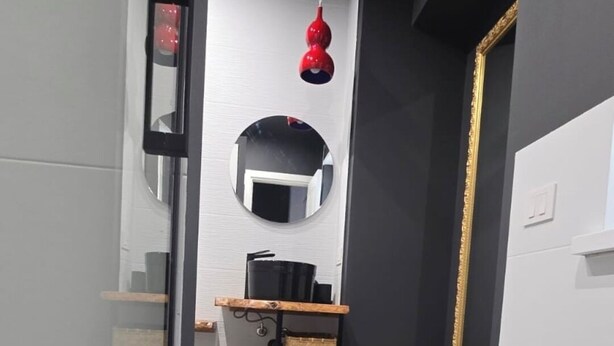 Une cuisine moderne dotée d’un four encastré, d’un luminaire rouge suspendu et d’un miroir placé au-dessus du plan de travail.