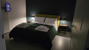 Un lit bien fait, avec une couvre-lit verte et des oreillers blancs, deux tables de chevet avec des lampes et un téléviseur fixé au mur.