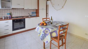 A compact kitchen with white cabinets, a gas stove, and a dining table set with a patterned tablecloth. - 4 bedroom amazing apartment in Ferruzzano (Ferruzzano)
