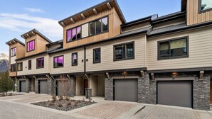 A modern multi-story residential building with a stone facade, large windows, and a paved driveway. - Luxury Modern Mountain Lodge in Spring Creek, Canmore (Canmore)