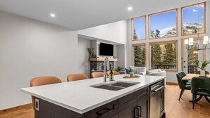 A modern kitchen with a large island, wooden cabinets, and a dining area with a view of trees. - Luxury Modern Mountain Lodge in Spring Creek, Canmore (Canmore)
