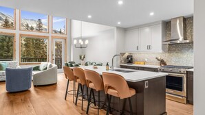 A modern kitchen with a central island, bar stools, and a dining area with a sofa and chairs. - Luxury Modern Mountain Lodge in Spring Creek, Canmore (Canmore)