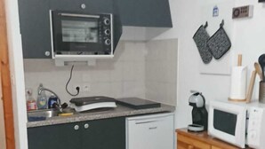 Cozinha compacta com micro-ondas, lava-louças e máquina de café. Há uma mesa de madeira e uma cadeira na área de refeições.
