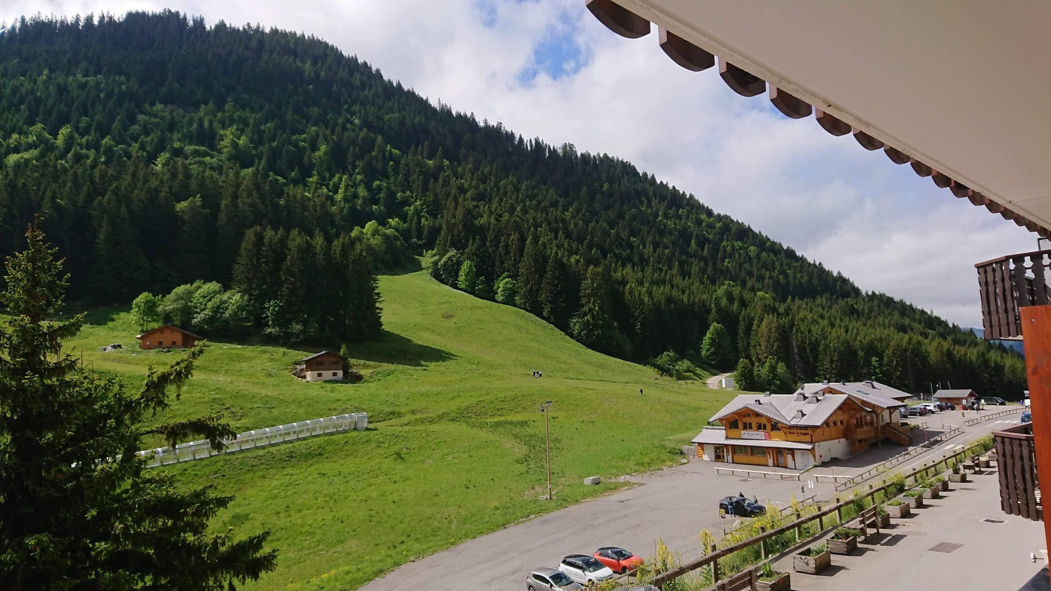 Un hotel con un’area di parcheggio, vista su una valle verde e una montagna boscosa sullo sfondo.
