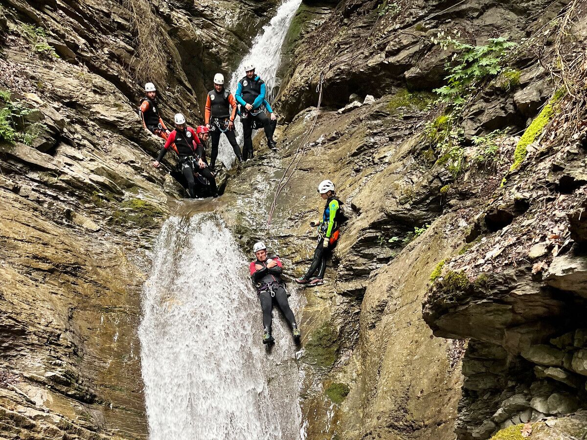 Un grupo de personas participa en una actividad acuática, posiblemente rafting o kayak, en un cañón rocoso con una cascada.