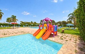 Ein Schwimmbad mit einer Wasserspielanlage für Kinder, Liegestühlen und Sonnenschirmen.