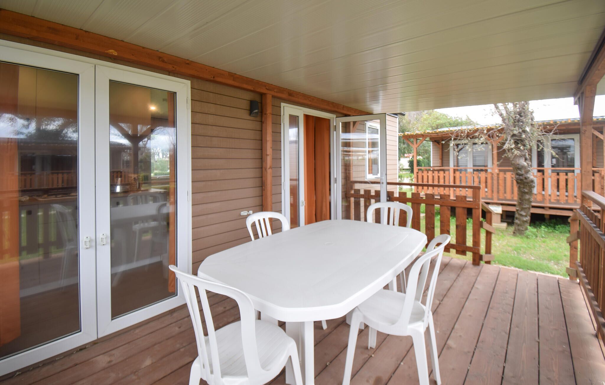 A covered patio with a white table and chairs, wooden deck, and a view of a wooden decked area in the background.