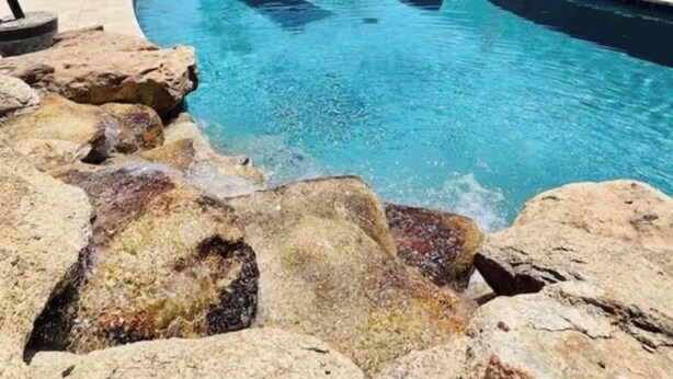 Ein Schwimmbecken mit klarem, blauem Wasser, umgeben von Felsen und Palmen.