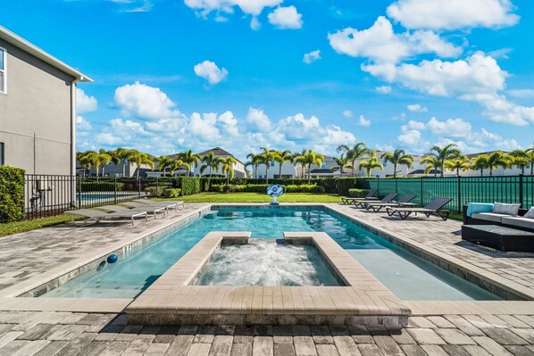 A swimming pool with a water feature, surrounded by lounge chairs and palm trees, with a clear sky above.