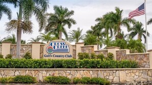 Bordje voor Cross Creek Golf & Country Club met palmbomen en een stenen muur op de voorgrond.
