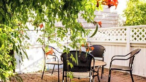Eine Terrasse im Freien mit einem weißen Spalierzaun, zwei Korbstühlen und einem Tisch.
