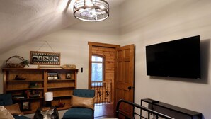 A bedroom with a bed, a TV, a bookshelf, and a wooden door leading to a balcony. - Secluded Mountain Cabin near Scenic Lakes & Trails (Hot Springs)