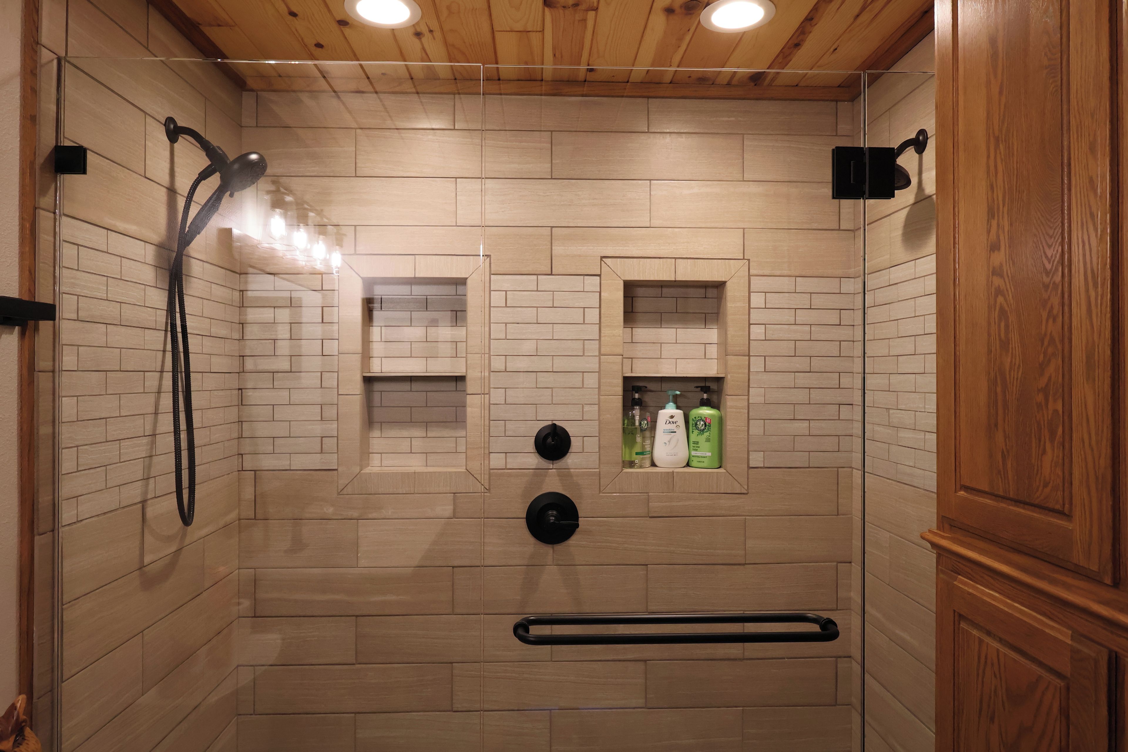 A shower area with a wooden ceiling, tiled walls, and a built-in shelf with toiletries.