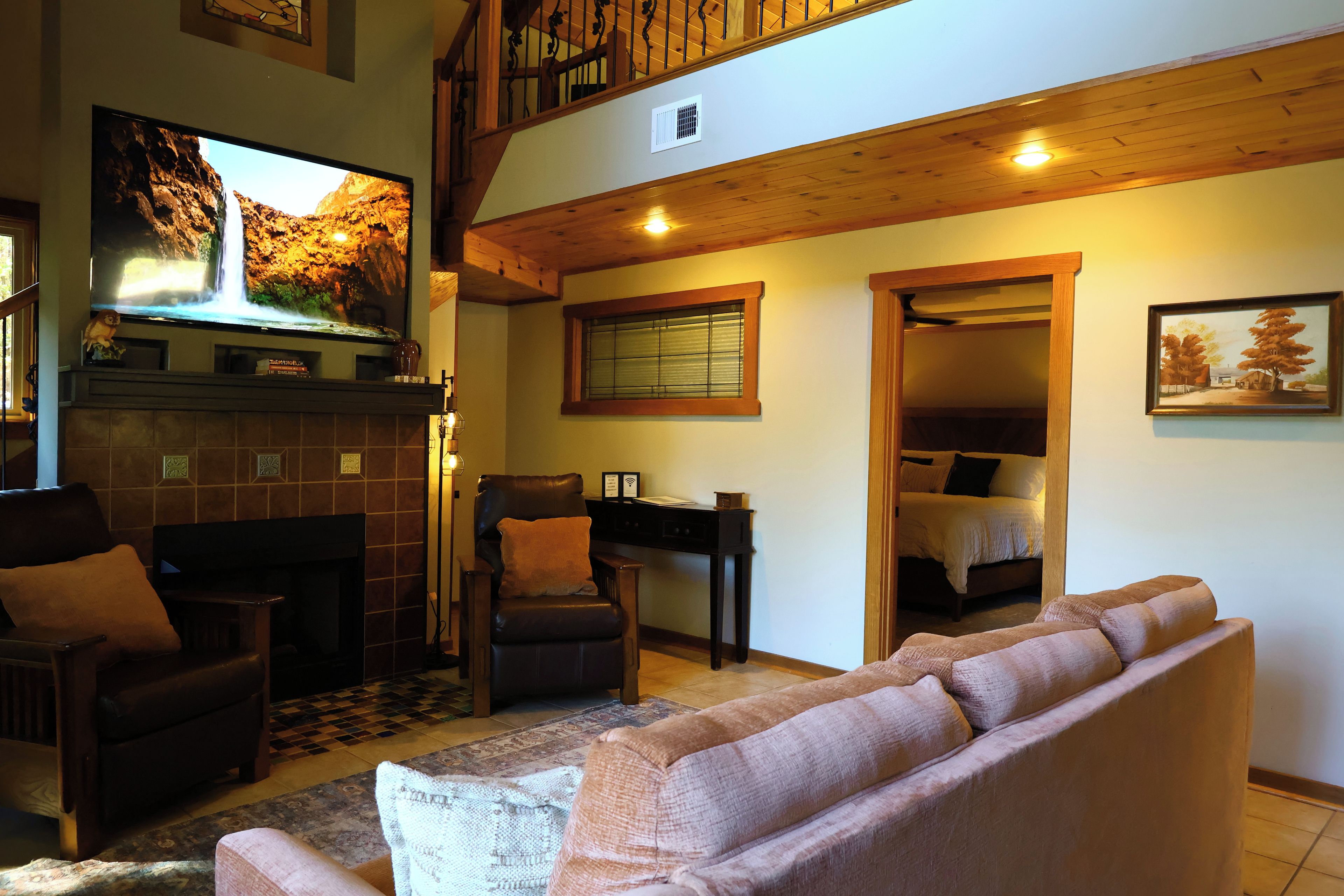 A living room with a fireplace, a television mounted on the wall, a sofa, and a dining area with a table and chairs.