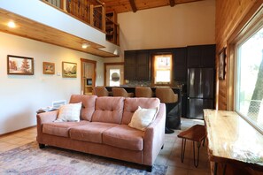 A cozy living room with a sofa, a dining table, and a kitchen in the background.