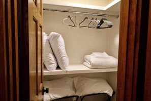 Ein Hotelzimmer mit einem Holzschrank, einem Bett mit weißer Bettwäsche und einem Regal mit gefalteten Handtüchern und Kleiderhaken.