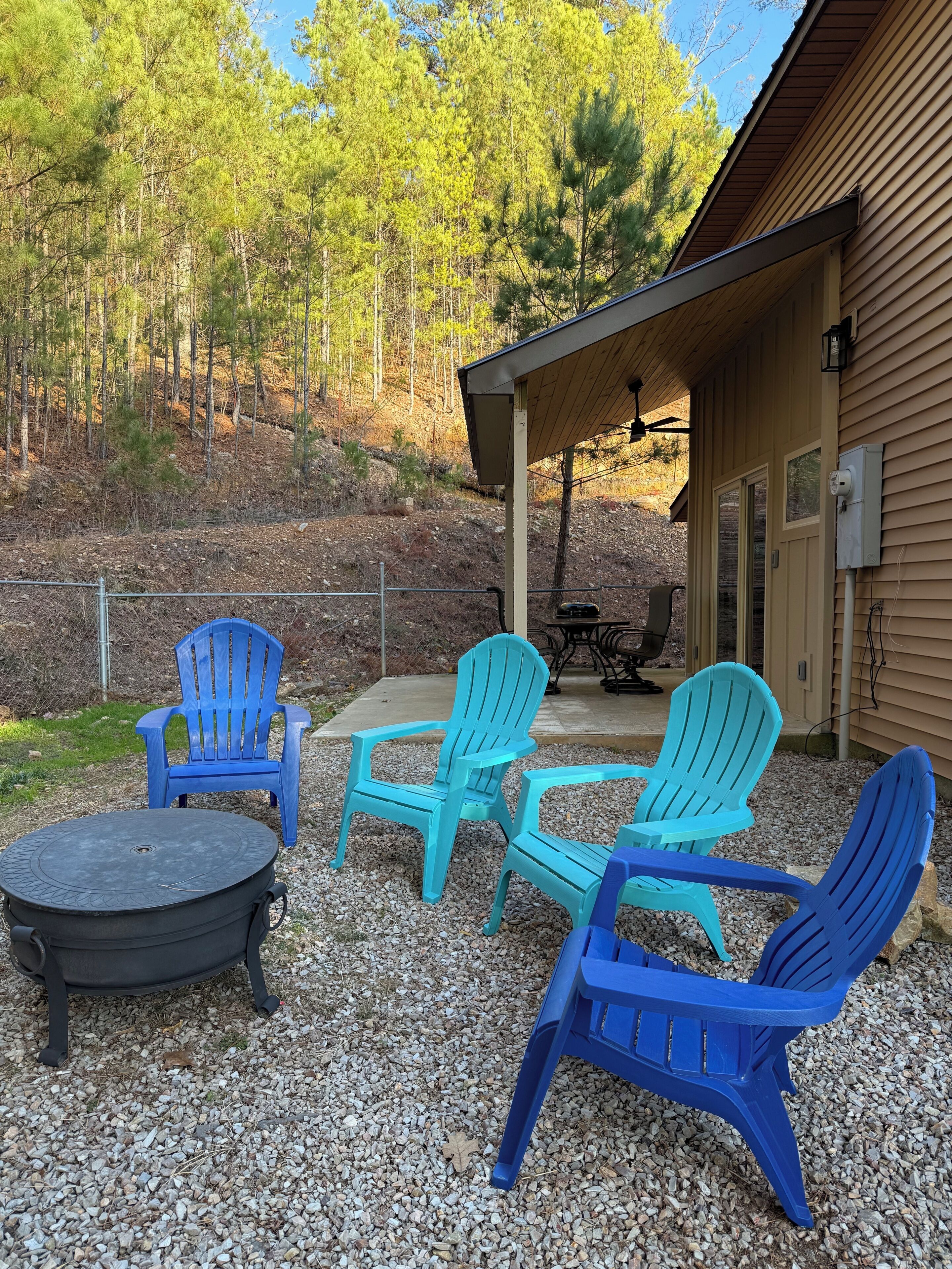 Een terras met vier blauwe Adirondack-stoelen en een ronde tafel, omringd door grind.